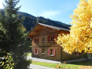 a small wooden house with red windows and a tree at Gästehaus zum Bären in Wald am Arlberg