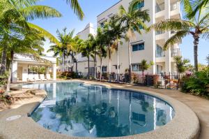 a swimming pool in front of a building with palm trees at Madison Ocean Breeze Apartments in Townsville