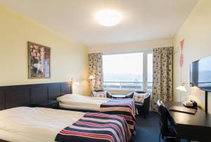 ニーネスハムンにあるスカルガーズホテレットのベッド2台、デスク、窓が備わるホテルルームです。