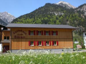a building with red windows and mountains in the background at Gästehaus zum Bären in Wald am Arlberg
