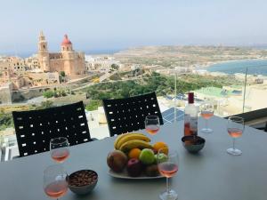 een tafel met een schaal fruit en wijnglazen bij Clifftop Modern Apartment in Mellieħa
