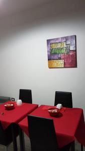Deux tables rouges avec des chaises et un tableau sur le mur dans l'établissement Domos Loru, à Sestu
