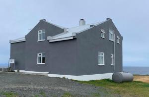 a large gray house with a barrel in front of it at Guesthouse Básar in Grímsey
