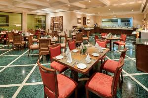 a restaurant with wooden tables and red chairs at The Lalit Temple View in Khajurāho