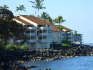 a building on the beach with palm trees and water at Sea Village 2nd floor Direct Oceanfront unit with extensive upgrades in Kailua-Kona