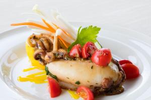 a white plate with a piece of food with vegetables on it at Lu' Hotel Porto Pino in SantʼAnna Arresi