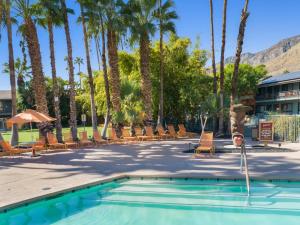 einen Pool mit Stühlen und Palmen in einem Resort in der Unterkunft Caliente Tropics in Palm Springs