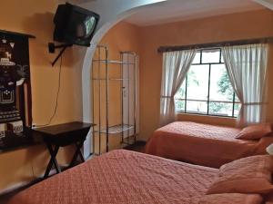a bedroom with two beds and a television and a window at El Pedron Hotel in Baños