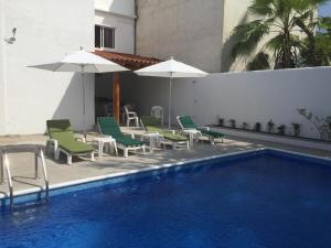 a pool with chairs and umbrellas next to a building at DEPARTAMENTOS LALO in Zihuatanejo