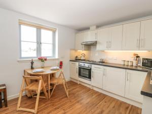 a kitchen with white cabinets and a wooden table at The Moorings in Isle of Whithorn