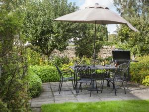 a table and chairs with an umbrella in a garden at Ellwood House in Caldbeck