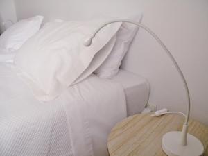 uma cama branca com um candeeiro branco sobre uma mesa de madeira em AL.Cova em Almada