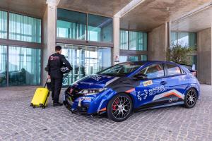 Un homme debout à côté d'une voiture bleue avec une valise jaune dans l'établissement Algarve Race Resort - Apartments, à Portimão