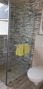 ein Bad mit einer Dusche, einem WC und gelben Handtüchern in der Unterkunft Ferienhäuser Oberdorla in Oberdorla