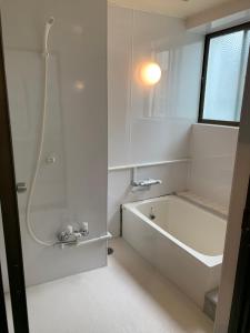 ein weißes Badezimmer mit einer Badewanne und einem Waschbecken in der Unterkunft ガナダン中央駅 2f 無料駐車場 in Kagoshima