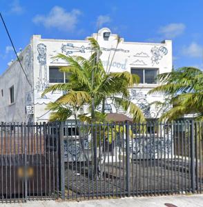 a building with palm trees in front of a fence at The Heart of Wynwood in Miami