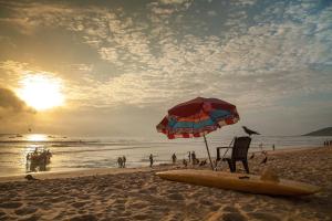 uma praia com um guarda-sol, uma cadeira e uma prancha de surf em O Camarao em Calangute