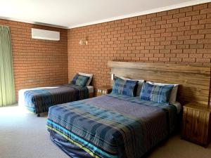 a bedroom with two beds and a brick wall at Kingswood Motel in Tocumwal