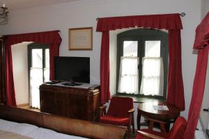 a bedroom with a bed and a tv and red curtains at Edvy Malom Fogadó Barokk Udvarház in Pápa