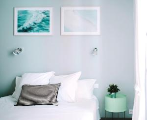 Outsite Coliving Biarritz في بياريتز: غرفة نوم بسرير ابيض مع وجود صورتين على الحائط