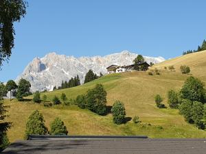 a house on a green hill with mountains in the background at Haus Anderl in Maria Alm am Steinernen Meer