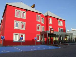 czerwony budynek z parkingiem przed nim w obiekcie Enzo Hotel Mulhouse Sud Morschwiller By Kyriad Direct w mieście Morschwiller-le-Bas