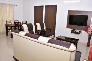 uma sala de estar com um sofá e cadeiras e uma televisão em Viswa Residency by Azalea em Madurai