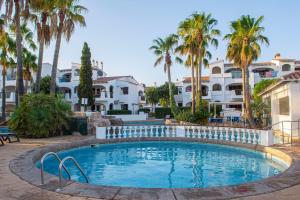 a swimming pool with palm trees and houses at Siesta Mar Apartamentos in Cala'n Porter