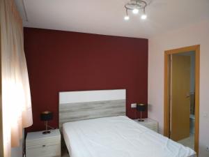 een slaapkamer met een wit bed en een rode muur bij Apartamento San Carlos de la Rápita in Sant Carles de la Ràpita