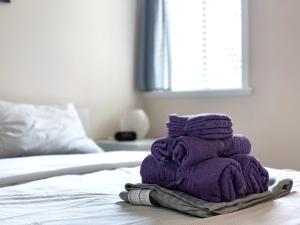 una pila de toallas púrpuras sentadas encima de una cama en Perfect Location - Tidy & Comfy Suite 5 Mins to Skytrain & Restaurant & Banks, 2 Stops To Metrotown, 5 Stops To Downtown, en Vancouver