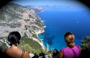 two women sitting on a cliff looking at the ocean at Hotel Bia Maore in Baunei