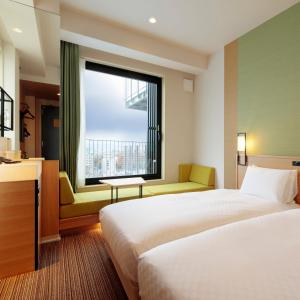 a hotel room with two beds and a window at Candeo Hotels Osaka Kishibe in Suita