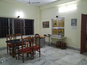 uma sala de jantar com mesa, cadeiras e janelas em Bhalobasa Anandabas em Bolpur