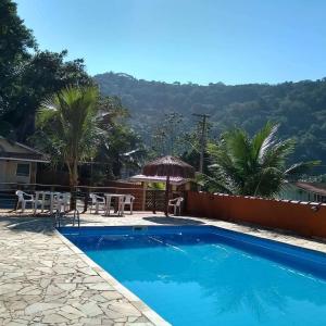 a pool with a table and chairs and mountains in the background at Chalé Residencial Bosque da Cocanha in Caraguatatuba