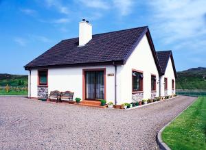 a white house with a bench on a gravel road at The Sheiling in Laide