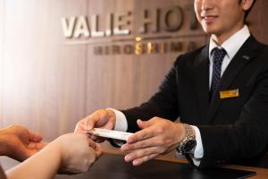 a man is handing a person a remote control at Valie Hotel Hiroshima in Hiroshima