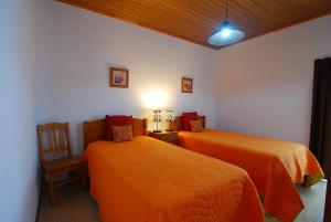 Faja GrandeにあるAlojamentos Flores Islandのベッドルーム1室(オレンジ色のベッド2台、椅子付)