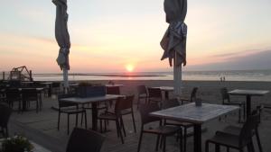a restaurant on the beach with tables and chairs and the sunset at ZeeBedStay in Noordwijk aan Zee