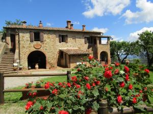モンテプルチャーノにあるAgriturismo Podere Fucileの赤いバラが目の前に広がる古い石造りの家