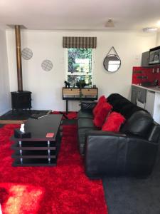 un soggiorno con divano in pelle nera e tappeto rosso di Hideaway - A Couples Retreat ad Akaroa