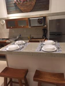 a kitchen with a counter with plates and stools at Praia do Forte Apartamento Fantástico in Praia do Forte