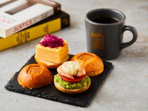 trois sandwichs sur une assiette à côté d'une tasse de café dans l'établissement LAMP LIGHT BOOKS HOTEL nagoya, à Nagoya