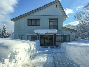 a house covered in snow with a driveway at Powder Peaks Chalet in Akakura