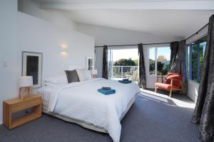 ein weißes Schlafzimmer mit einem großen Bett und einem Stuhl in der Unterkunft Waiheke Island Vineyard Holiday Houses in Surfdale