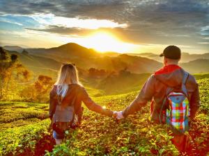 a man and woman walking through a field with the sun in the background at Oastel coLiving in Tanah Rata