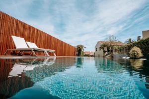 a swimming pool with two white chairs next to a wooden fence at Volcanic Charming House in Ribeira Grande