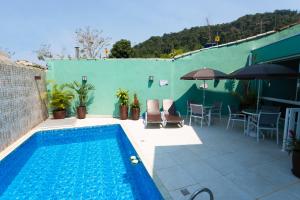 a swimming pool with chairs and a table and an umbrella at Pousada Pérola de Ubatuba in Ubatuba