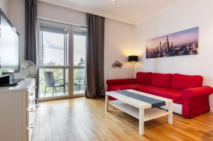 ワルシャワにあるGaleria Rondo Wiatraczna Apartmentsのリビングルーム(赤いソファ、テーブル付)