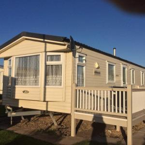 a wooden house with a porch and a fence at MV203 3 bedroom Deluxe caravan in Chapel Saint Leonards