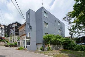 a gray building with a pointed roof on a street at Sakura Apartments in Kutchan